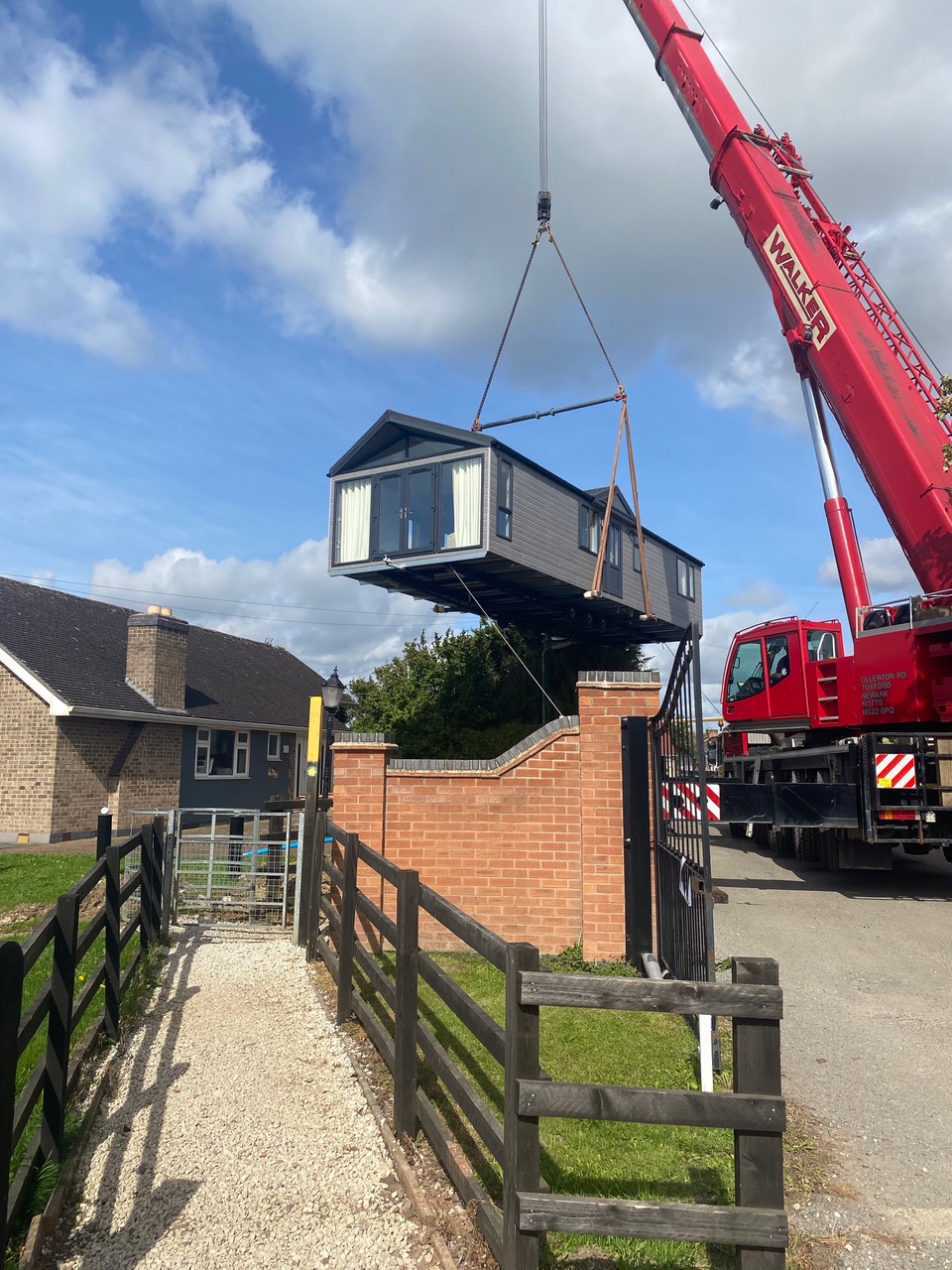 A static lodge being craned in over a gateway with dark post and rail fencing