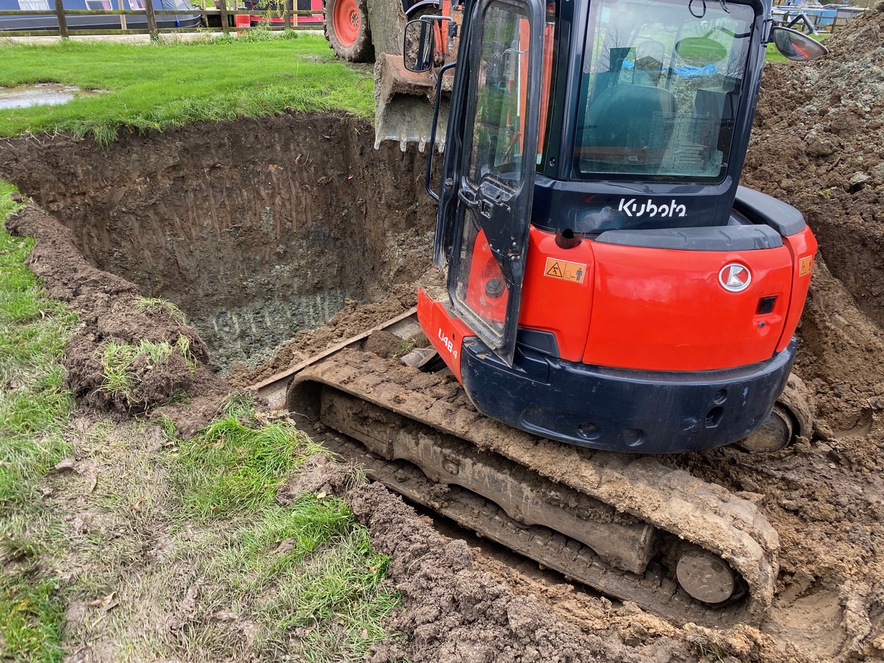 Kubota mini digger beside a deep excavation in a field